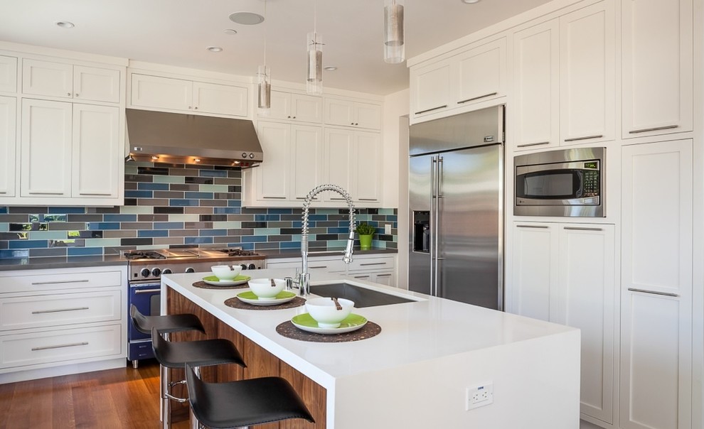 Inspiration for a transitional medium tone wood floor kitchen remodel with an undermount sink, shaker cabinets, white cabinets, laminate countertops, stainless steel appliances, an island, multicolored backsplash and mosaic tile backsplash