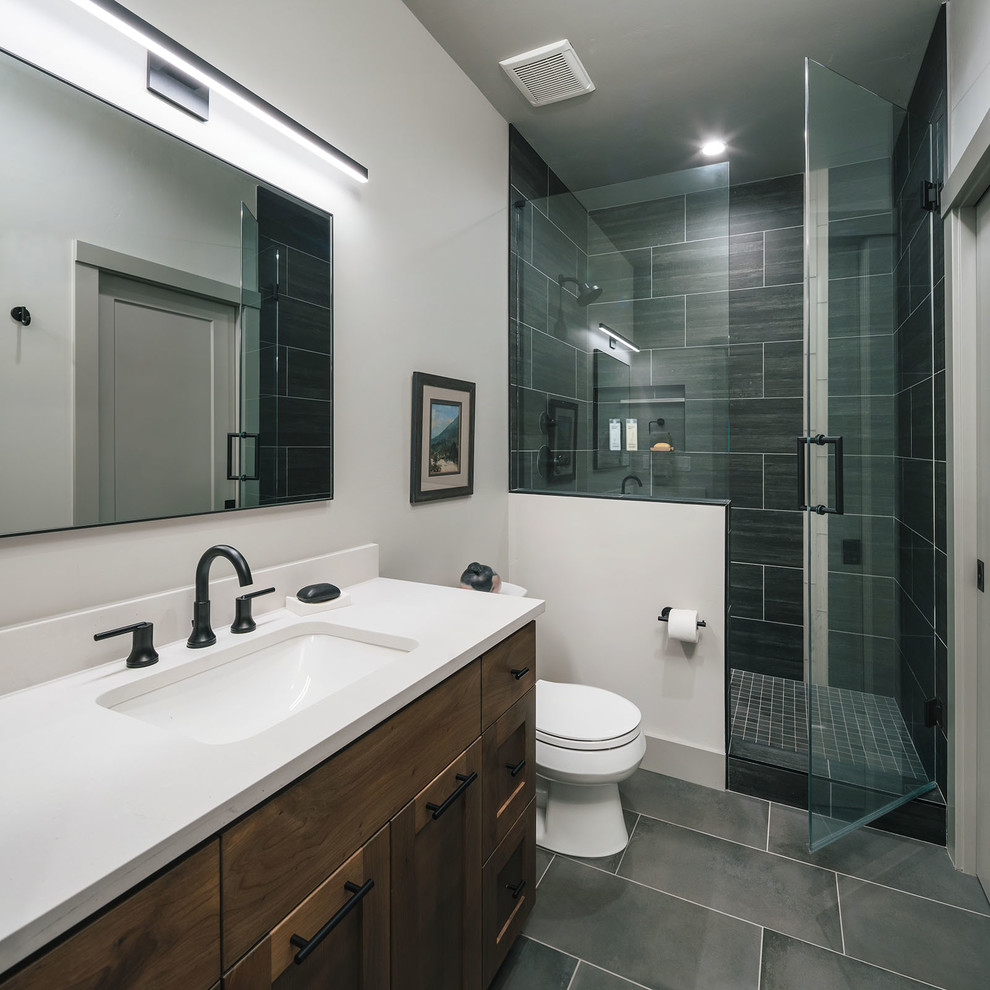 Inspiration for a mid-sized country 3/4 bathroom in Portland with shaker cabinets, brown cabinets, a corner shower, a one-piece toilet, gray tile, a drop-in sink, engineered quartz benchtops, a hinged shower door and white benchtops.