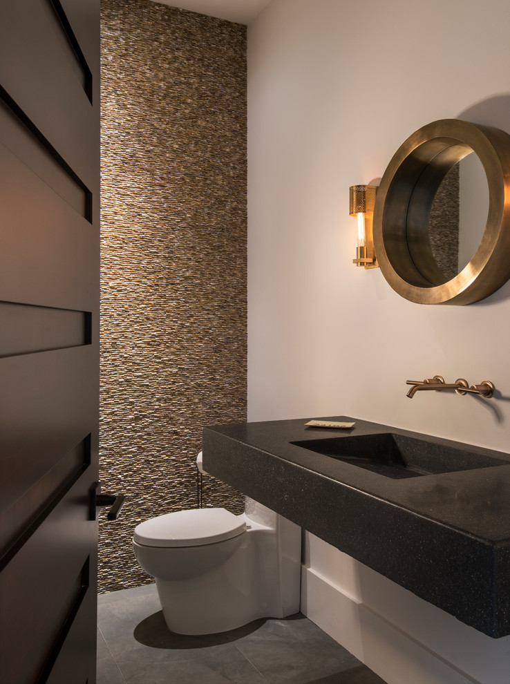 Design ideas for a small contemporary powder room in Miami with white walls, porcelain floors, a one-piece toilet, beige tile, stone tile, concrete benchtops, an integrated sink and black benchtops.