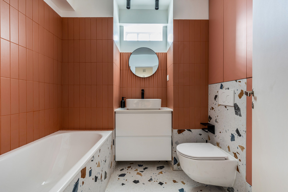 Inspiration for a medium sized retro ensuite bathroom in Paris with flat-panel cabinets, white cabinets, a submerged bath, a shower/bath combination, a wall mounted toilet, orange tiles, red tiles, ceramic tiles, orange walls, light hardwood flooring, a built-in sink, multi-coloured floors, white worktops, a single sink, a floating vanity unit and a hinged door.