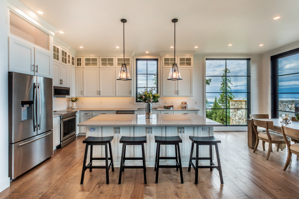 Large transitional l-shaped medium tone wood floor and brown floor eat-in kitchen photo with quartzite countertops, wood backsplash, stainless steel appliances, an island, gray countertops, an undermount sink, shaker cabinets, white cabinets and white backsplash