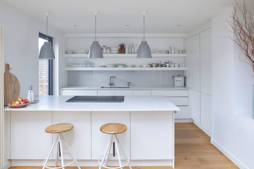 Design ideas for a mid-sized contemporary u-shaped kitchen in London with an undermount sink, flat-panel cabinets, white cabinets, white splashback, glass sheet splashback, panelled appliances, medium hardwood floors, a peninsula, beige floor and white benchtop.