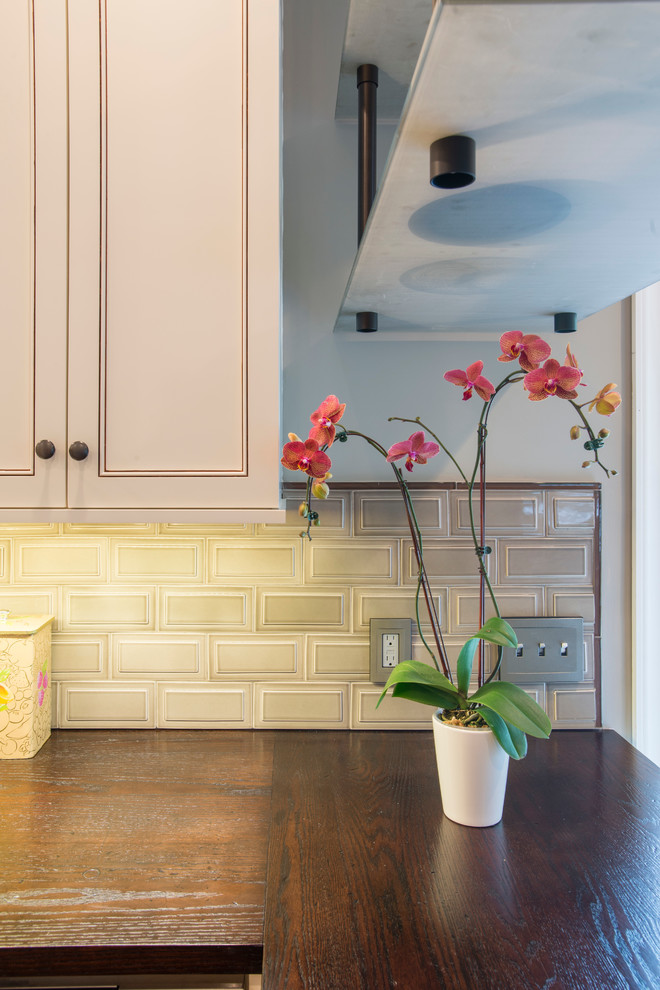 Example of a mid-sized transitional u-shaped medium tone wood floor eat-in kitchen design in New York with an undermount sink, recessed-panel cabinets, white cabinets, granite countertops, beige backsplash, subway tile backsplash, stainless steel appliances and a peninsula