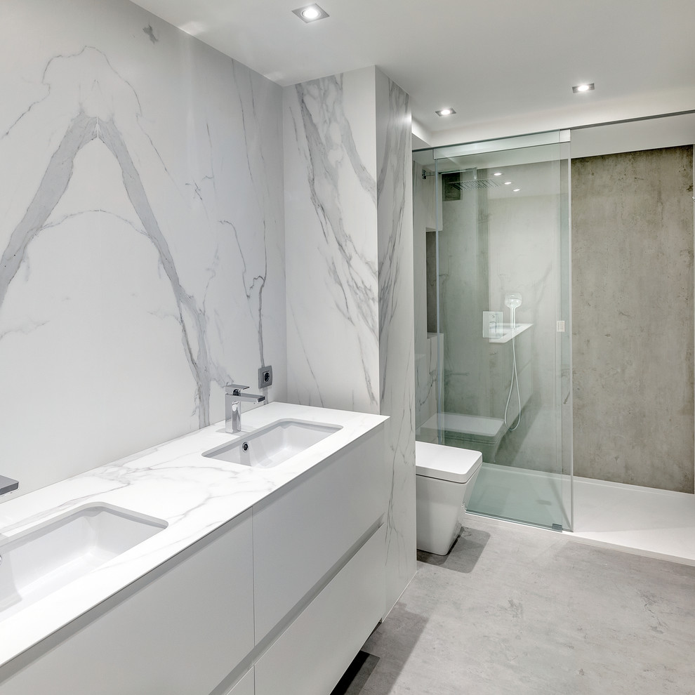 Photo of a contemporary kids bathroom in Essex with flat-panel cabinets, white cabinets, an open shower, a wall-mount toilet, white tile, marble, white walls, an integrated sink, marble benchtops, grey floor and a sliding shower screen.