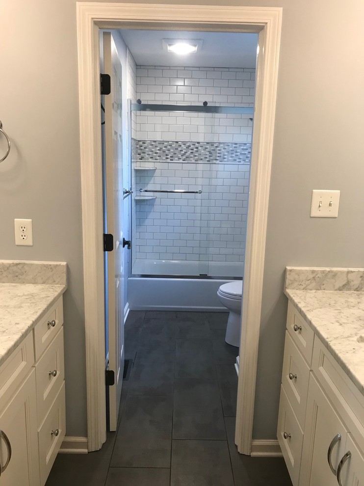 This is an example of a mid-sized transitional 3/4 bathroom in Indianapolis with recessed-panel cabinets, white cabinets, an alcove tub, a shower/bathtub combo, a two-piece toilet, white tile, subway tile, grey walls, slate floors, an undermount sink, granite benchtops, grey floor, a sliding shower screen and white benchtops.