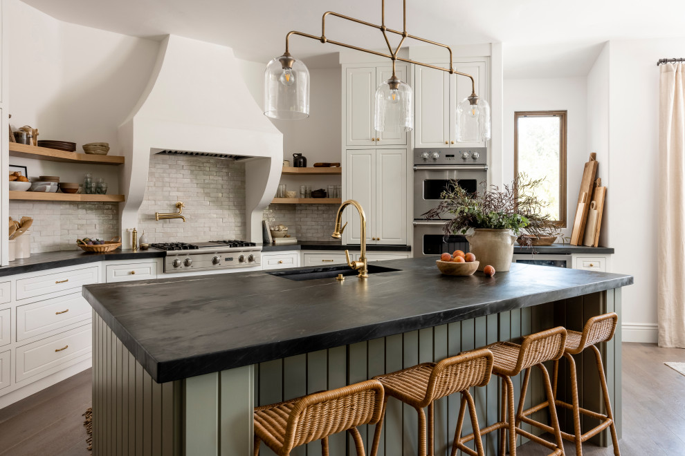 Country u-shaped eat-in kitchen in Sacramento with an undermount sink, raised-panel cabinets, white cabinets, marble benchtops, grey splashback, stainless steel appliances, medium hardwood floors, with island, brown floor and black benchtop.