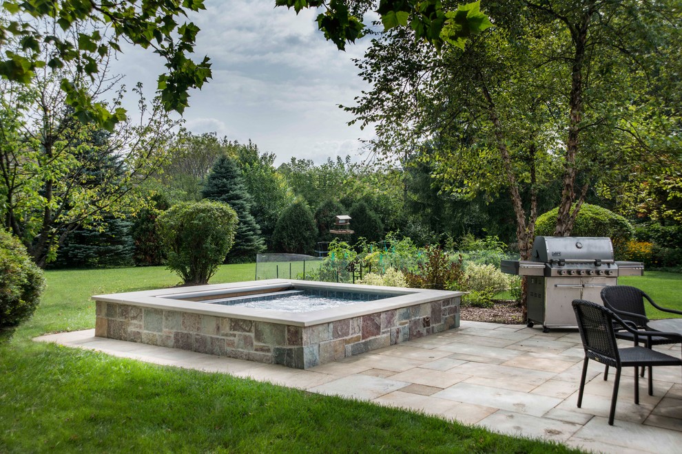 This is an example of a small country backyard rectangular natural pool in Chicago with a hot tub and natural stone pavers.