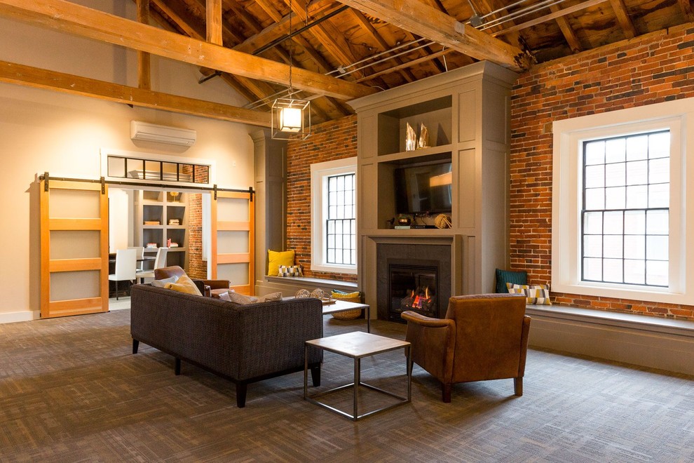 This is an example of a large industrial loft-style living room in Boston with beige walls, carpet, a standard fireplace, a plaster fireplace surround and grey floor.