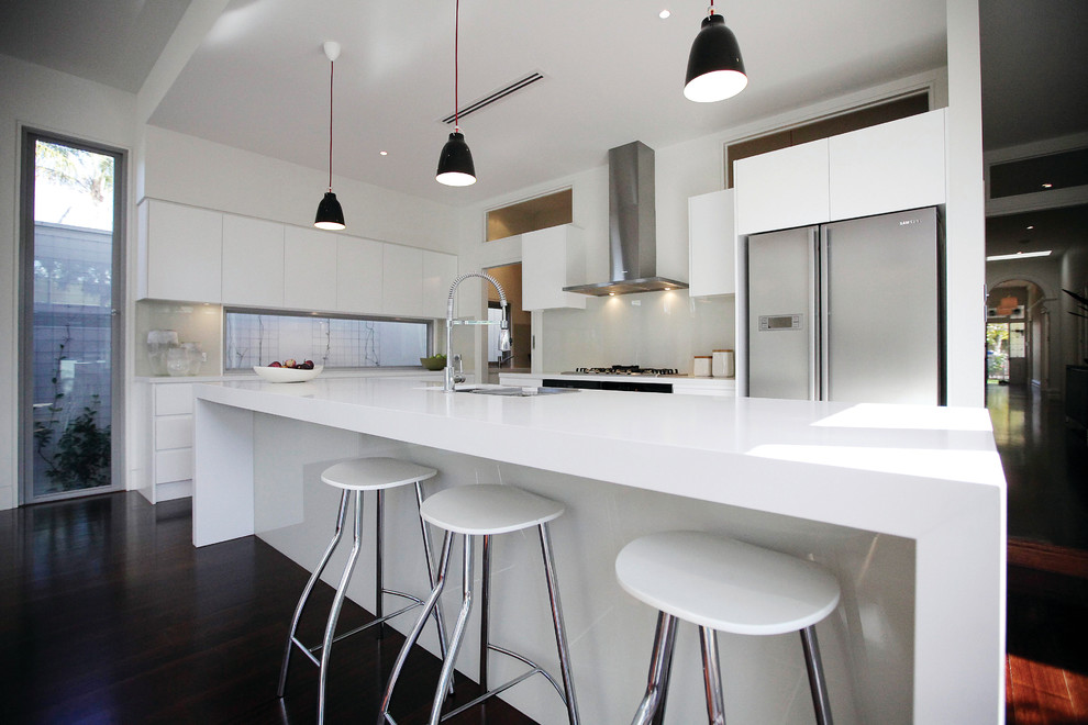 Large contemporary galley kitchen pantry in Melbourne with an undermount sink, flat-panel cabinets, white cabinets, quartz benchtops, white splashback, glass sheet splashback, stainless steel appliances, dark hardwood floors and with island.