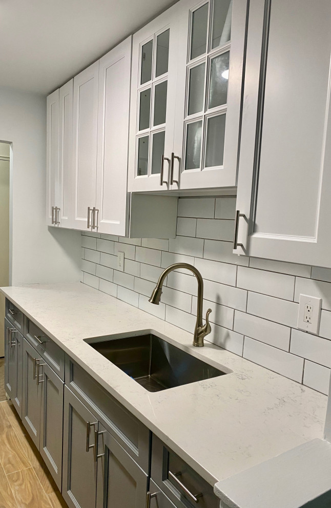 Photo of a small country galley separate kitchen in New York with an undermount sink, shaker cabinets, white cabinets, quartz benchtops, white splashback, subway tile splashback, stainless steel appliances, ceramic floors, beige floor and white benchtop.