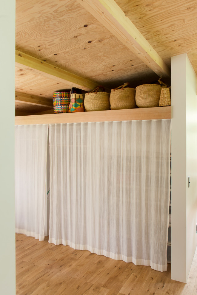 Immagine di armadi e cabine armadio unisex minimalisti di medie dimensioni con ante bianche, pavimento in legno massello medio e travi a vista