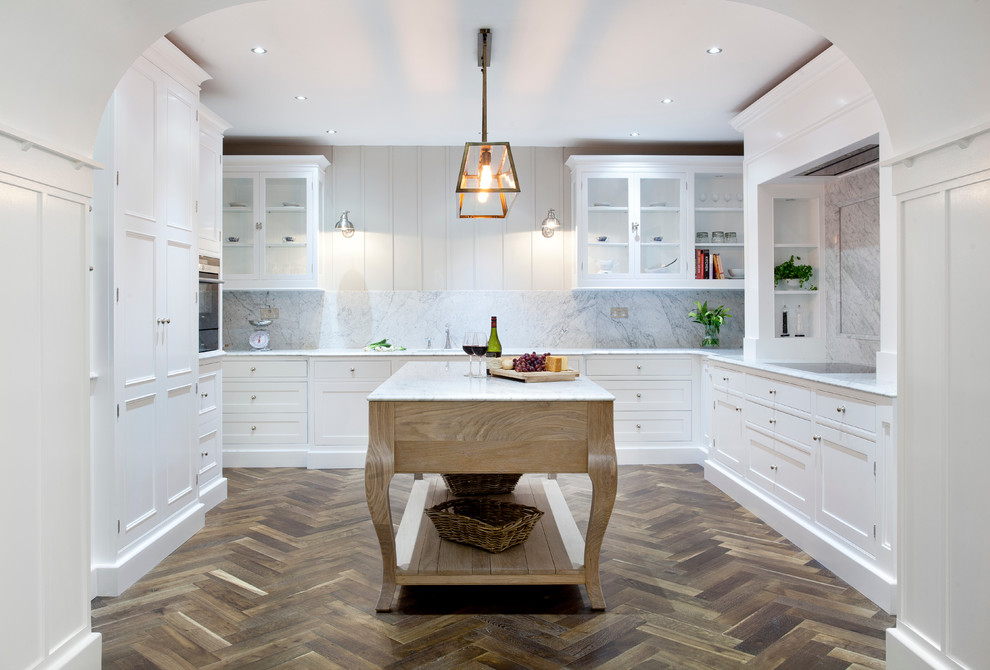 This is an example of a large transitional u-shaped kitchen in Dublin with an undermount sink, beaded inset cabinets, white cabinets, marble benchtops, white splashback, stone slab splashback, stainless steel appliances, dark hardwood floors and with island.