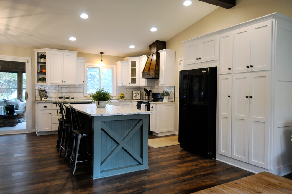 Photo of a large country l-shaped eat-in kitchen in Minneapolis with a farmhouse sink, shaker cabinets, white cabinets, quartz benchtops, white splashback, subway tile splashback, black appliances, dark hardwood floors, with island, brown floor and white benchtop.