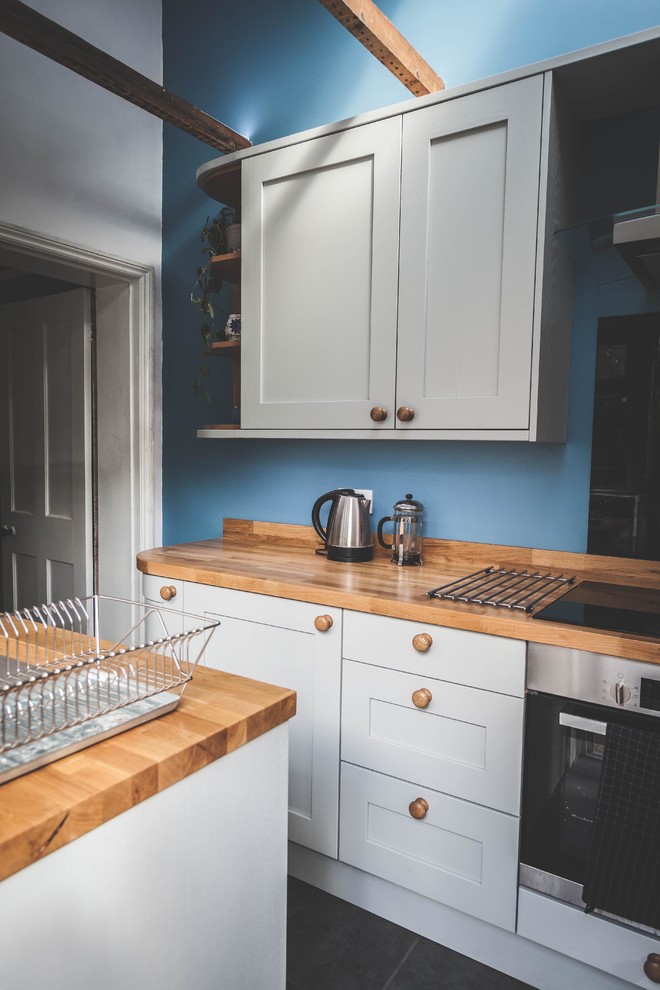 Design ideas for a small traditional l-shaped separate kitchen in Devon with a drop-in sink, shaker cabinets, grey cabinets, wood benchtops, black splashback, glass sheet splashback, panelled appliances, no island and grey floor.