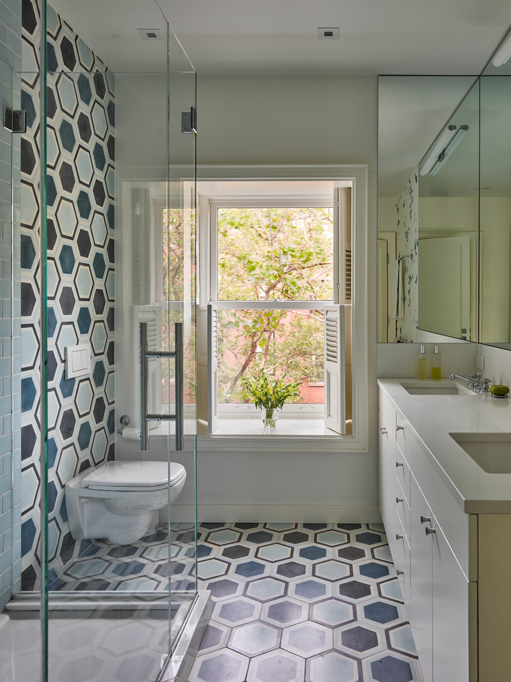 Inspiration for a transitional 3/4 bathroom in New York with flat-panel cabinets, beige cabinets, a corner shower, a wall-mount toilet, blue tile, grey walls, ceramic floors, an undermount sink, a hinged shower door and beige benchtops.