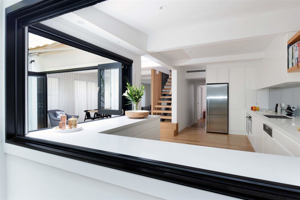 Inspiration for a mid-sized contemporary u-shaped open plan kitchen in Sydney with a double-bowl sink, flat-panel cabinets, white cabinets, solid surface benchtops, stainless steel appliances, light hardwood floors, brown floor and white benchtop.