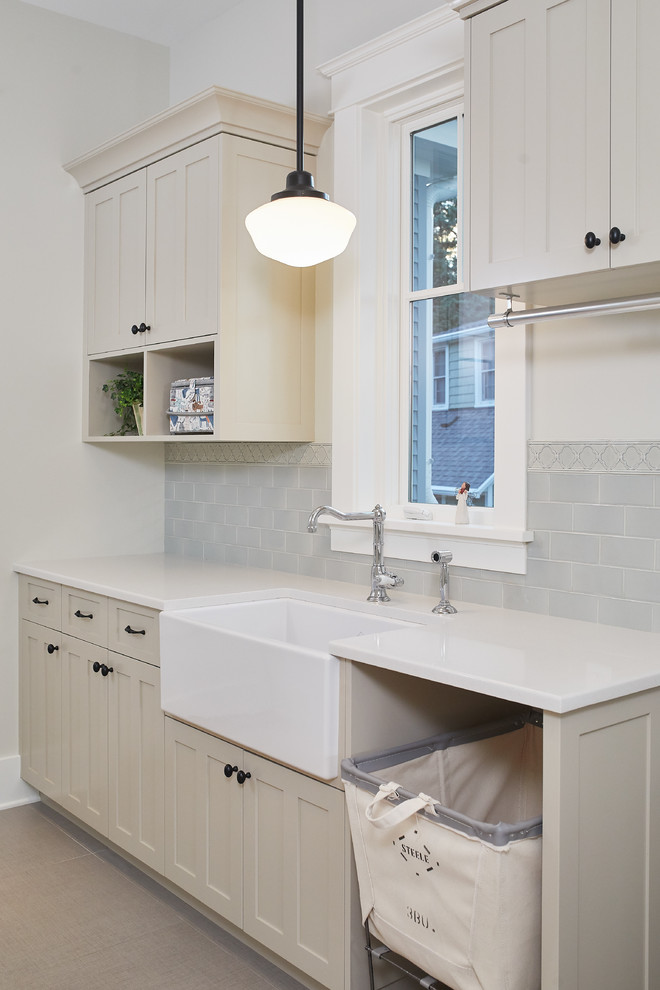 Inspiration for a country single-wall dedicated laundry room in Grand Rapids with a farmhouse sink, shaker cabinets, beige cabinets, brown floor, white benchtop, solid surface benchtops and grey walls.