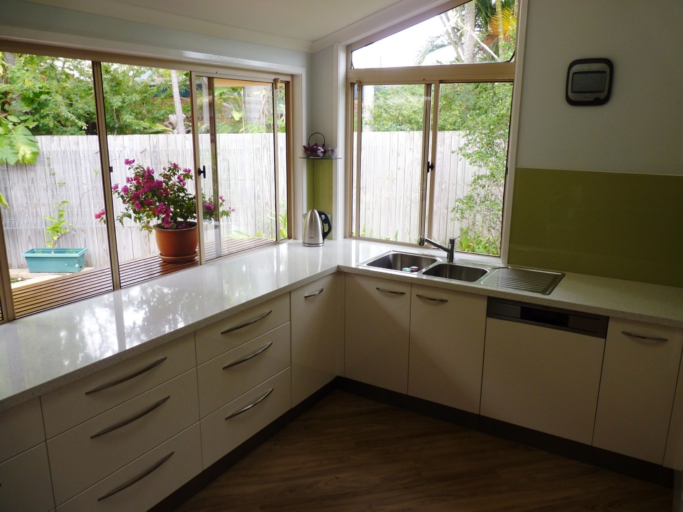 Inspiration for a mid-sized modern u-shaped kitchen in Sunshine Coast with a drop-in sink, flat-panel cabinets, white cabinets, quartz benchtops, green splashback, glass sheet splashback and stainless steel appliances.