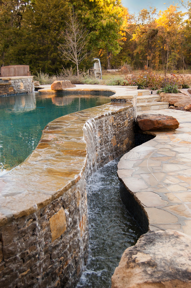 Design ideas for a mid-sized country backyard custom-shaped infinity pool in Other with a water feature and natural stone pavers.