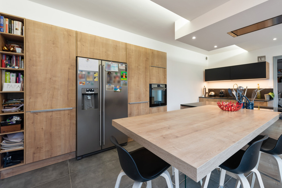 Inspiration for a mid-sized contemporary l-shaped eat-in kitchen in Lyon with travertine floors, beige floor, flat-panel cabinets, medium wood cabinets, with island, an undermount sink, black splashback, slate splashback, stainless steel appliances and black benchtop.
