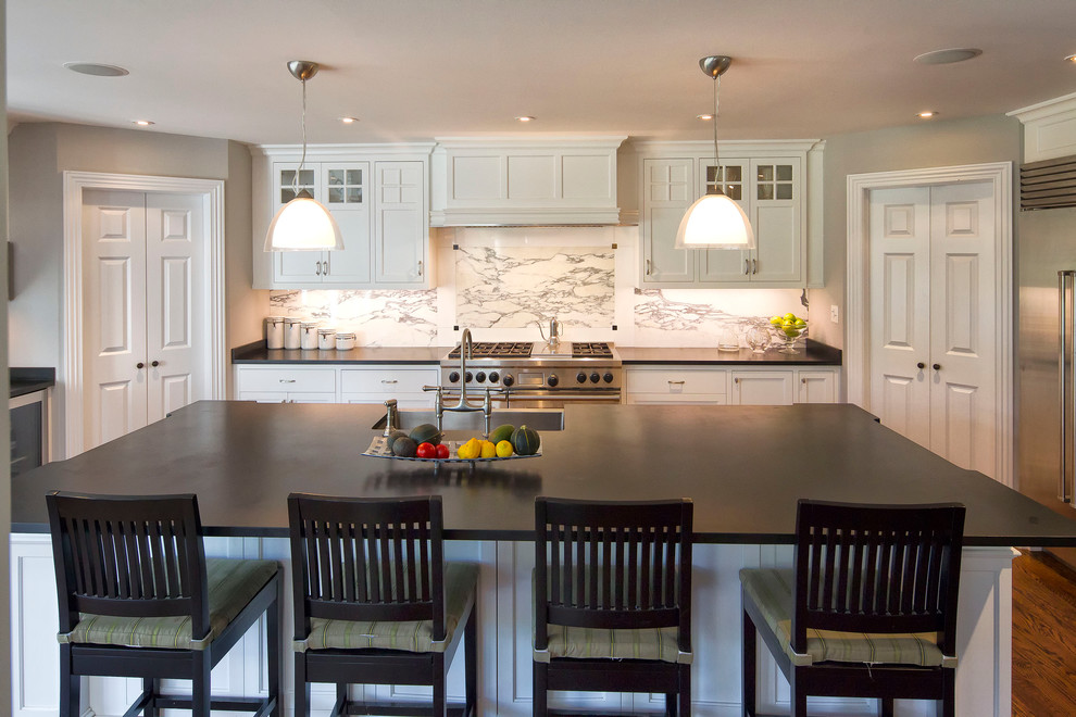Photo of a traditional u-shaped open plan kitchen in New York with a farmhouse sink, beaded inset cabinets, white cabinets, granite benchtops, white splashback, marble splashback, stainless steel appliances, medium hardwood floors, with island and black benchtop.