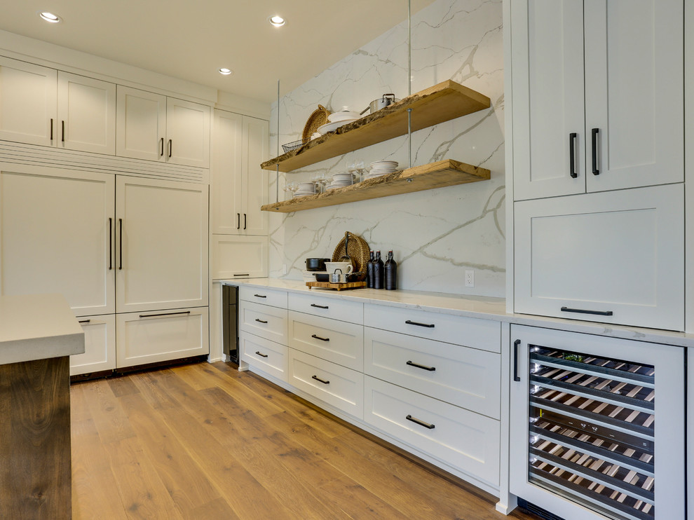 Inspiration for an expansive country u-shaped open plan kitchen in Portland with a farmhouse sink, shaker cabinets, white cabinets, quartz benchtops, white splashback, stone slab splashback, panelled appliances, medium hardwood floors, with island and brown floor.