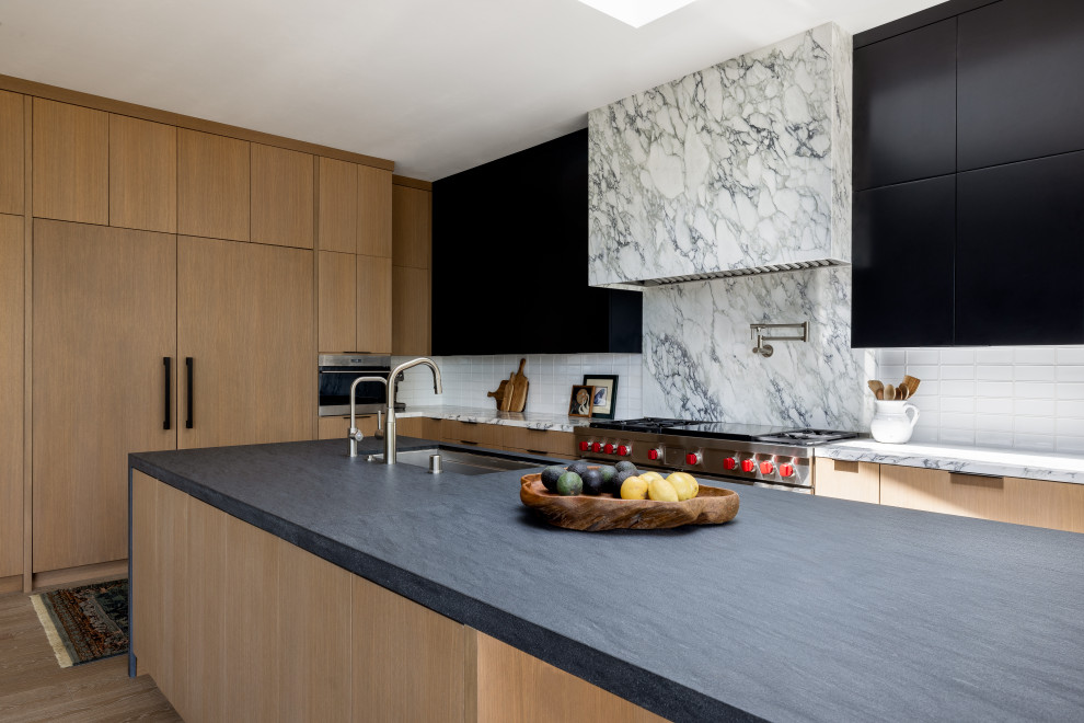 Exempel på ett stort modernt svart svart kök, med en nedsänkt diskho, släta luckor, svarta skåp, bänkskiva i täljsten, vitt stänkskydd, stänkskydd i marmor, rostfria vitvaror, ljust trägolv, en köksö och brunt golv