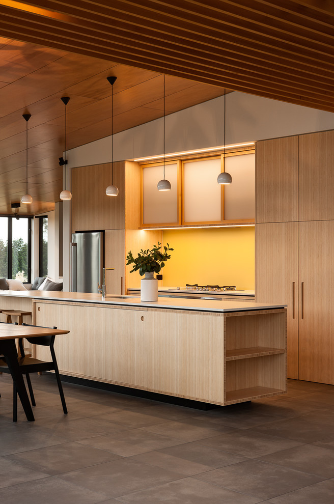 Photo of a mid-sized contemporary galley eat-in kitchen in Auckland with raised-panel cabinets, light wood cabinets, yellow splashback, glass sheet splashback, stainless steel appliances, porcelain floors and with island.
