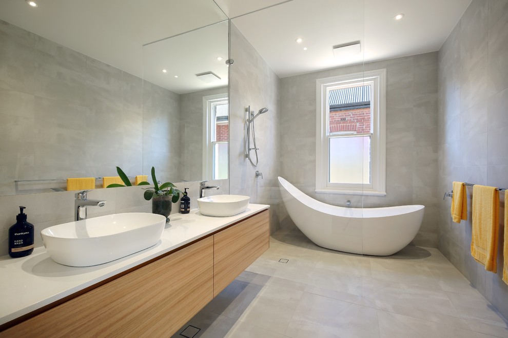 Photo of a mid-sized contemporary master wet room bathroom in Adelaide with light wood cabinets, a freestanding tub, gray tile, ceramic tile, ceramic floors, engineered quartz benchtops, grey floor, an open shower, white benchtops, flat-panel cabinets and a vessel sink.