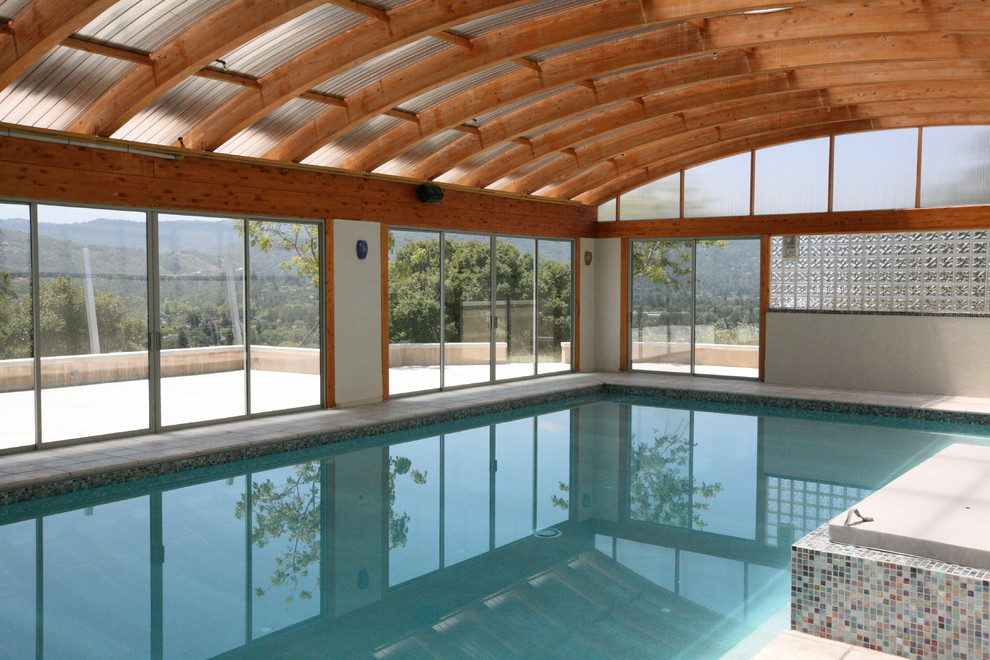 This is an example of an expansive contemporary indoor rectangular pool in San Francisco with a pool house and natural stone pavers.