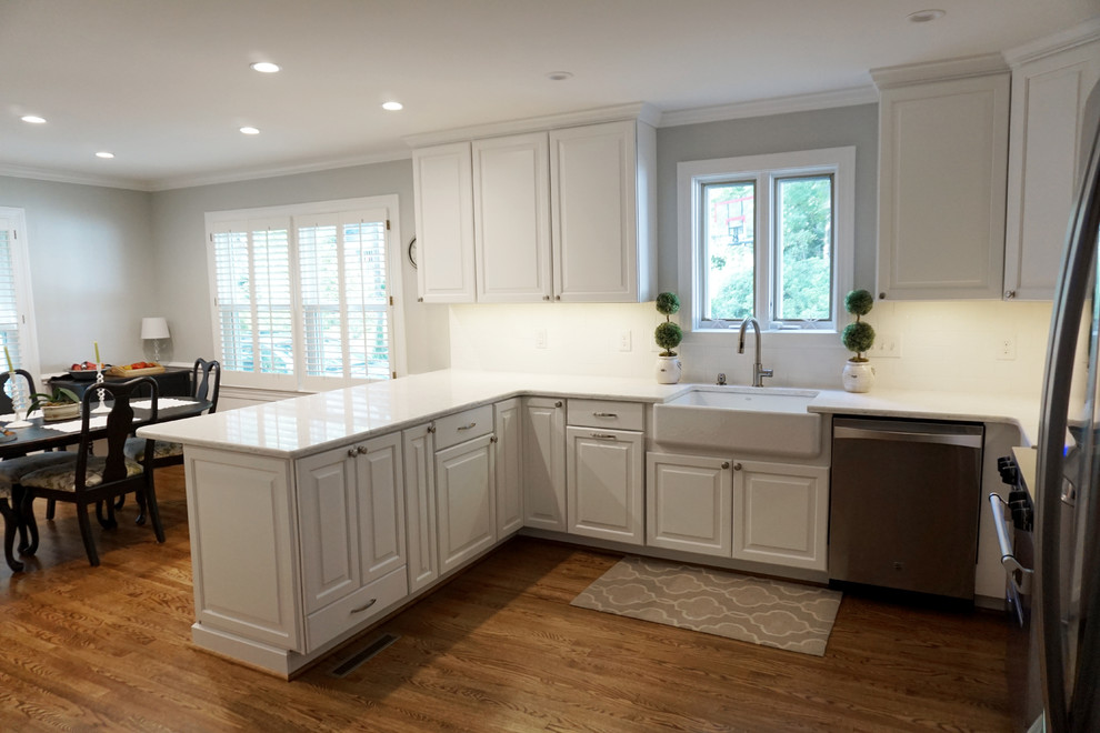 Photo of a mid-sized country u-shaped eat-in kitchen in Charlotte with a farmhouse sink, shaker cabinets, white cabinets, quartzite benchtops, white splashback, ceramic splashback, stainless steel appliances, medium hardwood floors and a peninsula.