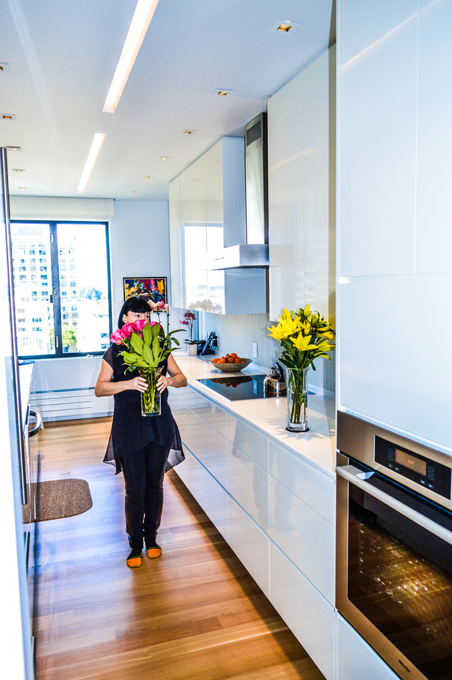 This is an example of a small modern galley enclosed kitchen in San Francisco with a submerged sink, flat-panel cabinets, yellow cabinets, quartz worktops, yellow splashback, glass tiled splashback, stainless steel appliances, light hardwood flooring and white worktops.