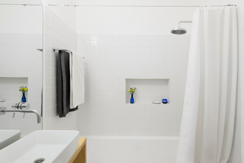 Photo of a small contemporary master bathroom in Tel Aviv with open cabinets, light wood cabinets, wood benchtops, a wall-mount toilet, white tile, ceramic tile, white walls, concrete floors and an alcove tub.
