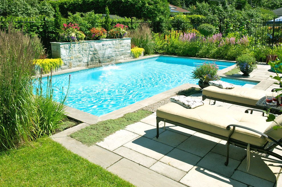 Photo of a mid-sized traditional backyard rectangular natural pool in Montreal with a water feature and concrete pavers.