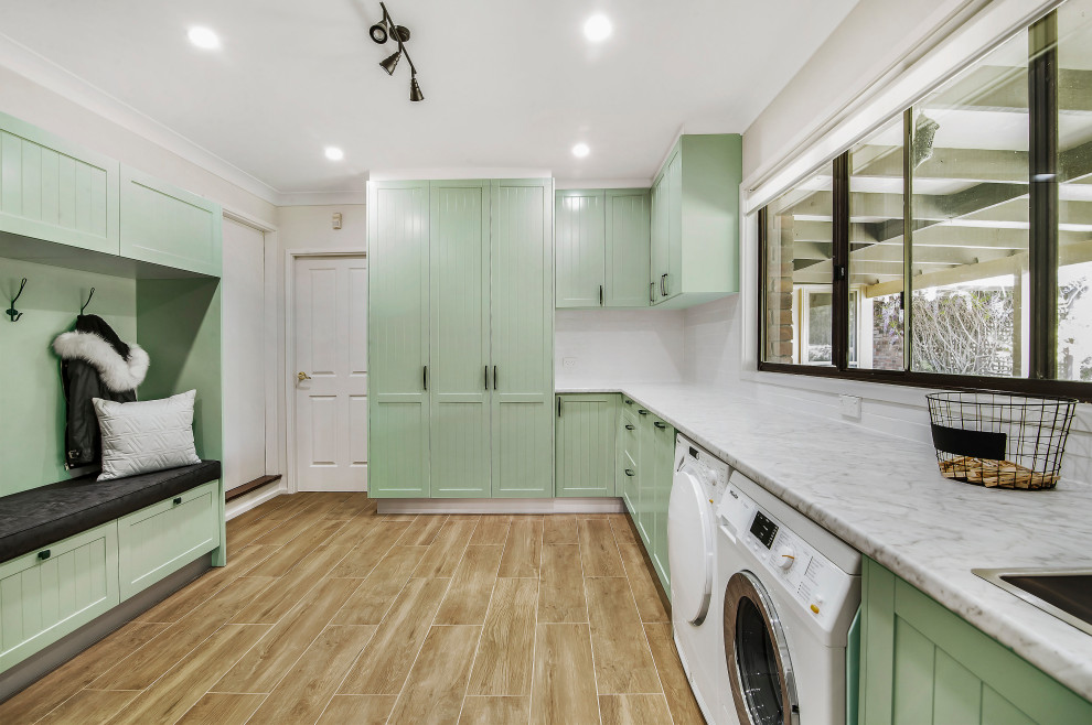 Design ideas for a transitional l-shaped utility room in Sydney with shaker cabinets, green cabinets, laminate benchtops, grey walls, porcelain floors, a side-by-side washer and dryer, brown floor and a drop-in sink.