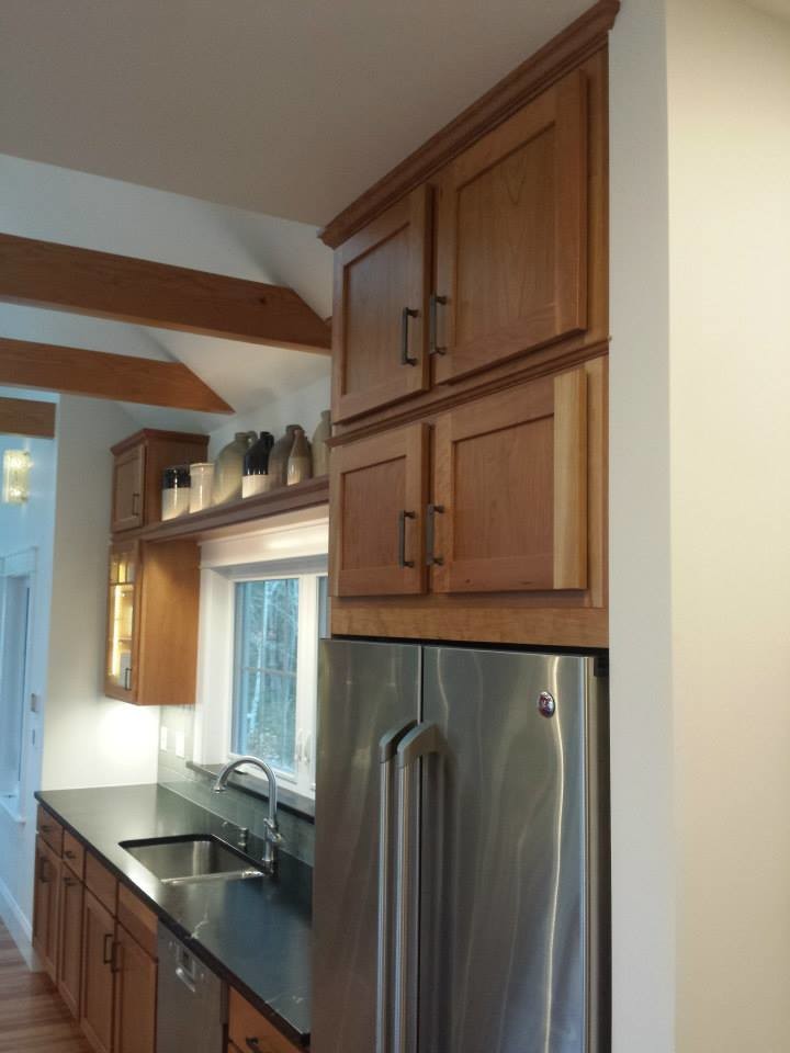 Large transitional medium tone wood floor and brown floor kitchen photo with an undermount sink, shaker cabinets, medium tone wood cabinets, soapstone countertops, stainless steel appliances and black countertops