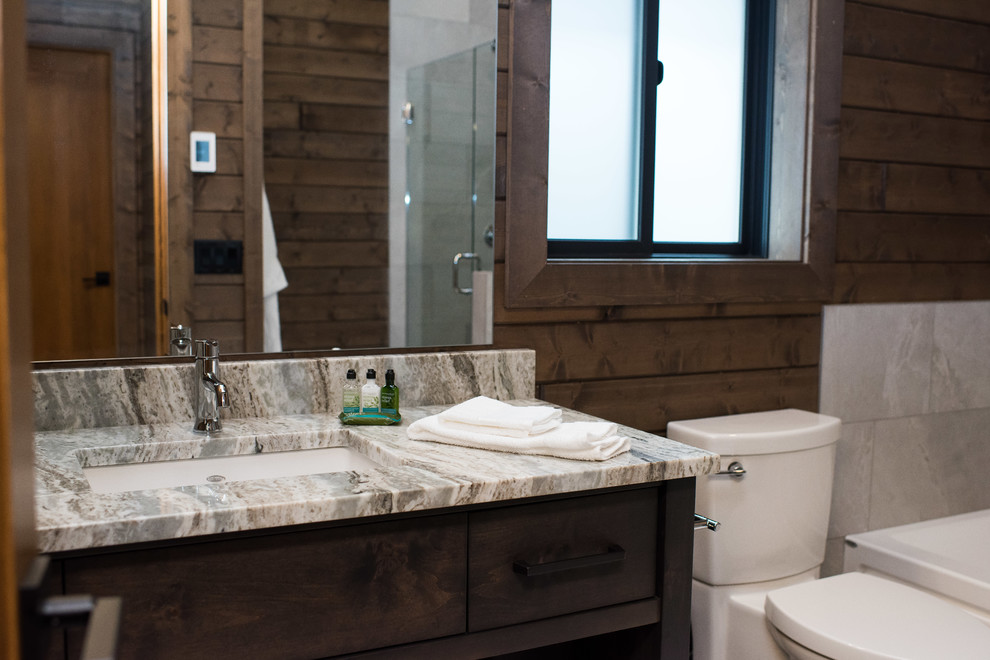 This is an example of a country master bathroom in Vancouver with shaker cabinets, light wood cabinets, gray tile, ceramic tile, granite benchtops, grey benchtops, an alcove tub, an alcove shower, a two-piece toilet, brown walls, ceramic floors, an undermount sink, grey floor and a hinged shower door.