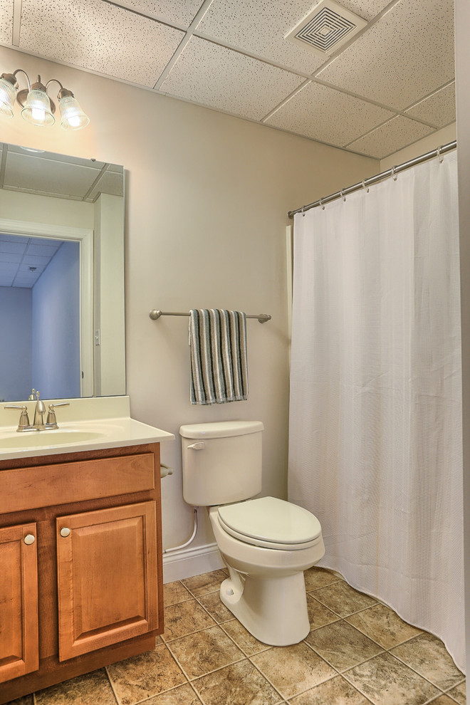 Mid-sized contemporary bathroom in Other with an integrated sink, raised-panel cabinets, medium wood cabinets, solid surface benchtops, a shower/bathtub combo, a two-piece toilet, multi-coloured tile, ceramic tile, white walls and ceramic floors.