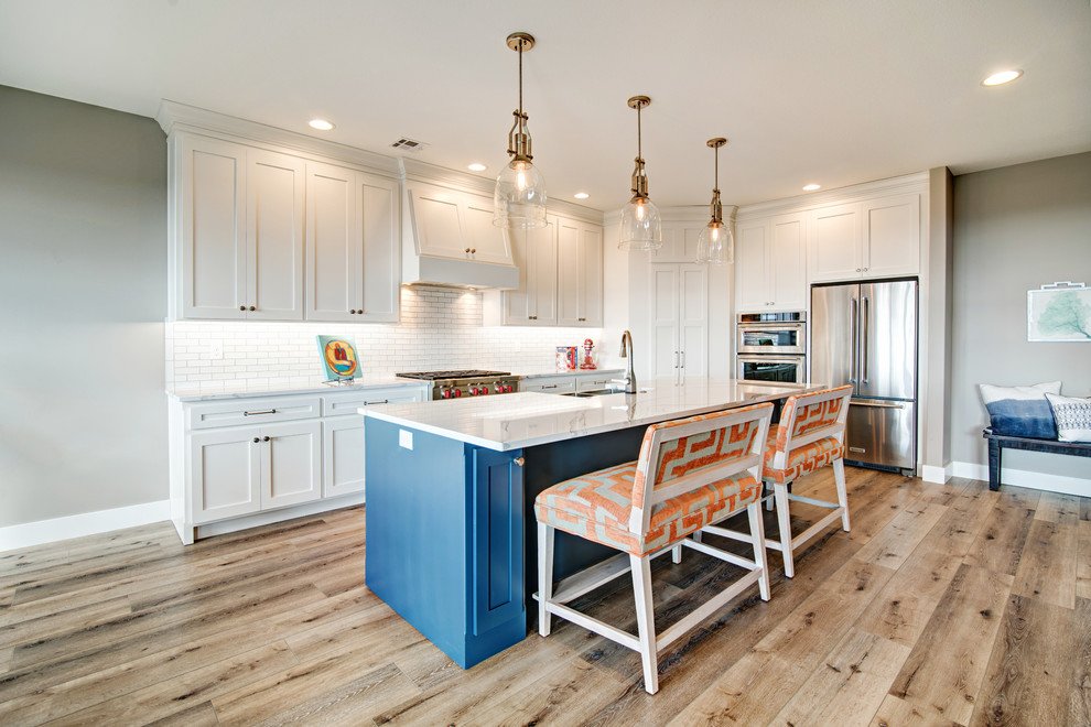 Photo of a large beach style l-shaped eat-in kitchen in Other with shaker cabinets, blue cabinets, quartz benchtops, white splashback, stainless steel appliances, medium hardwood floors, with island, brown floor, a double-bowl sink and subway tile splashback.