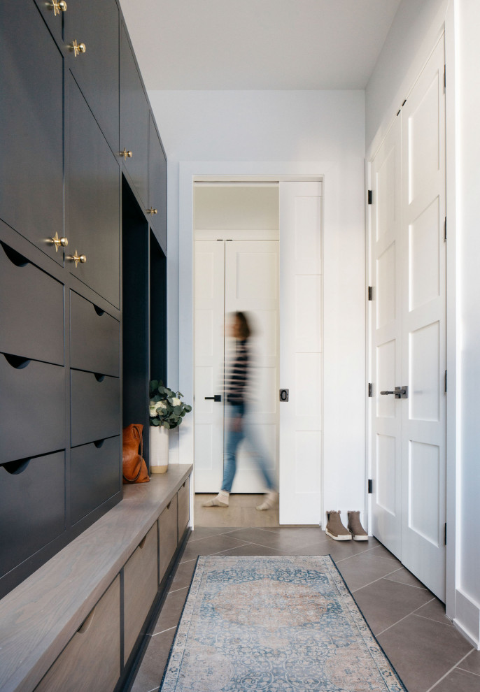 Cette image montre une grande buanderie linéaire minimaliste multi-usage avec un placard à porte plane, des portes de placard noires, un mur blanc et un sol marron.