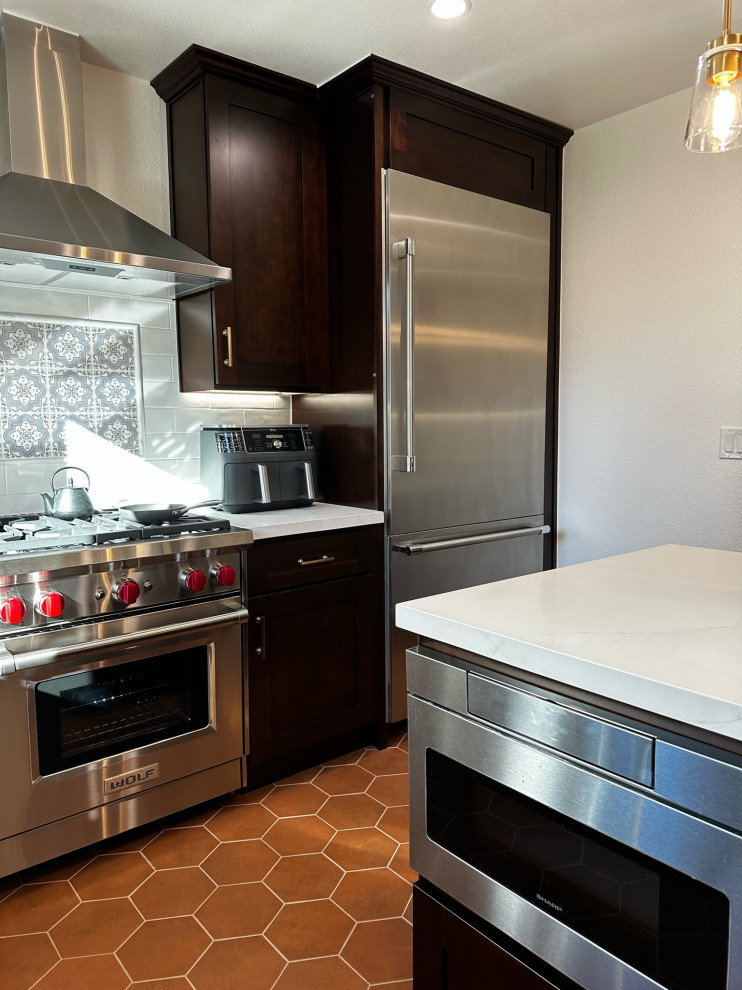 Bild på ett stort amerikanskt vit vitt kök, med en rustik diskho, skåp i shakerstil, skåp i mörkt trä, bänkskiva i kvartsit, vitt stänkskydd, stänkskydd i keramik, rostfria vitvaror, klinkergolv i keramik, en köksö och brunt golv