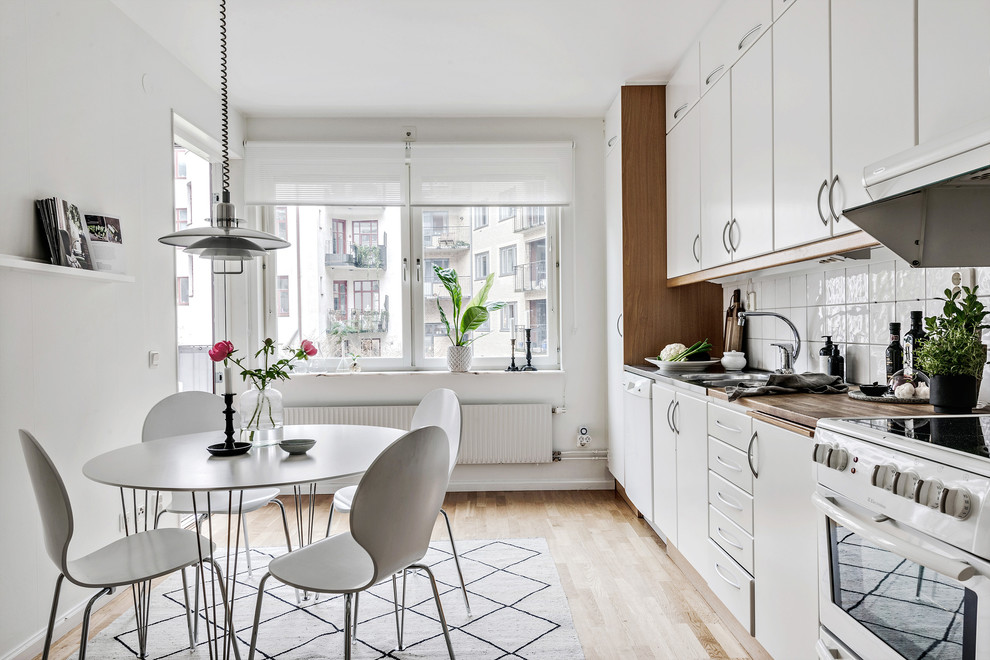 Design ideas for a scandinavian single-wall eat-in kitchen in Gothenburg with white cabinets, no island, an integrated sink, flat-panel cabinets, wood benchtops, white splashback, white appliances, light hardwood floors, beige floor and brown benchtop.
