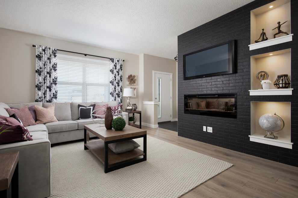 Mid-sized modern open concept family room in Calgary with black walls, laminate floors, a hanging fireplace, a brick fireplace surround, a wall-mounted tv and brown floor.