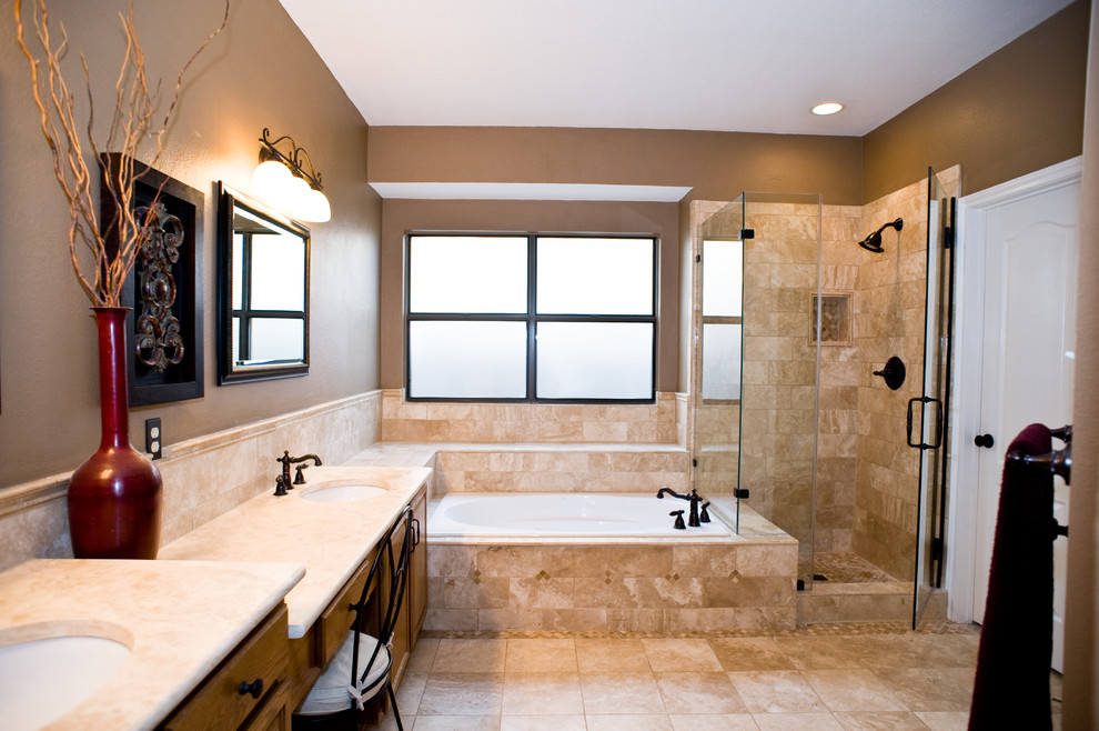 Photo of a large traditional master bathroom in Austin with raised-panel cabinets, medium wood cabinets, an undermount tub, a corner shower, beige tile, stone tile, brown walls, travertine floors, an undermount sink and granite benchtops.