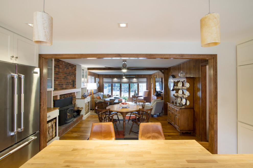 This is an example of a mid-sized traditional open plan dining in New York with brown walls, light hardwood floors, a standard fireplace, a brick fireplace surround and brown floor.
