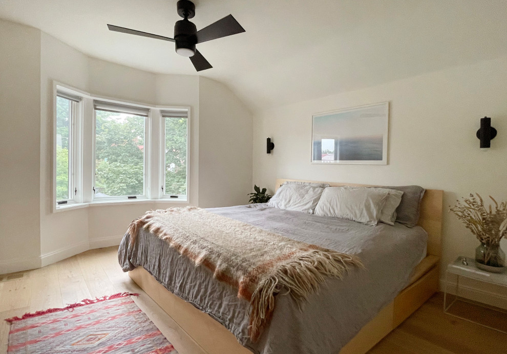This is an example of a modern master bedroom in Toronto with white walls, light hardwood floors and brown floor.