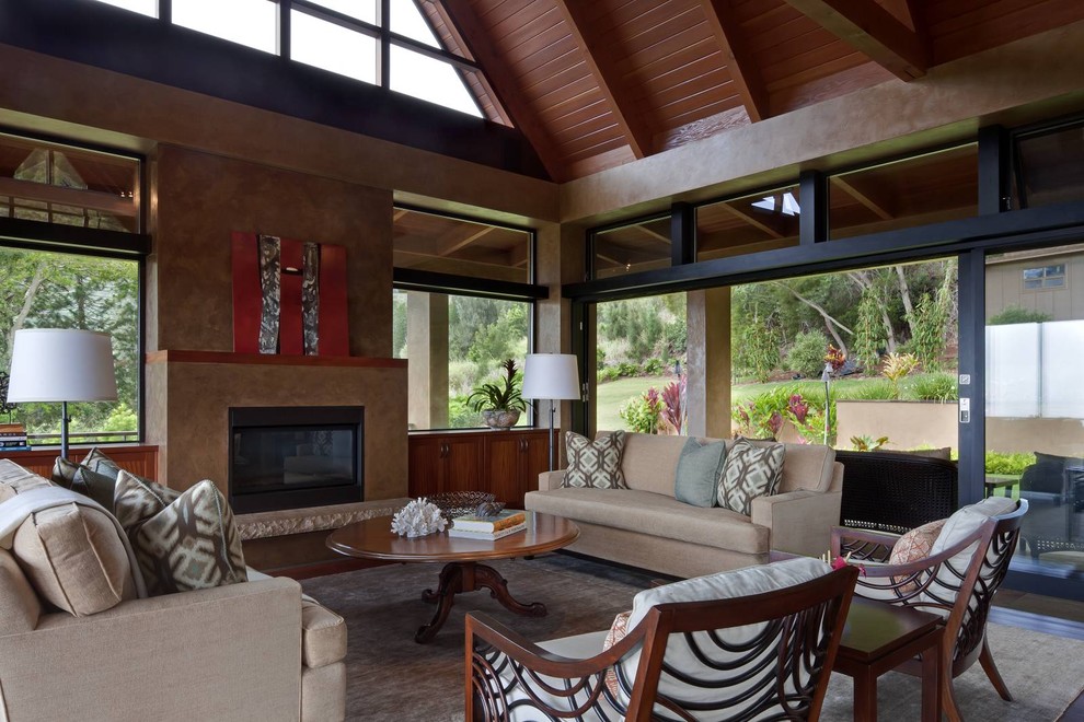 This is an example of a large tropical open concept living room in Hawaii with beige walls, dark hardwood floors, a standard fireplace, a plaster fireplace surround, no tv and brown floor.