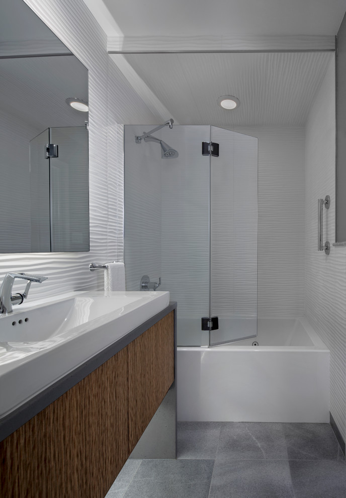Inspiration for a small modern 3/4 bathroom in Detroit with flat-panel cabinets, medium wood cabinets, an alcove tub, a shower/bathtub combo, a wall-mount toilet, white tile, ceramic tile, grey walls, marble floors, a vessel sink and solid surface benchtops.