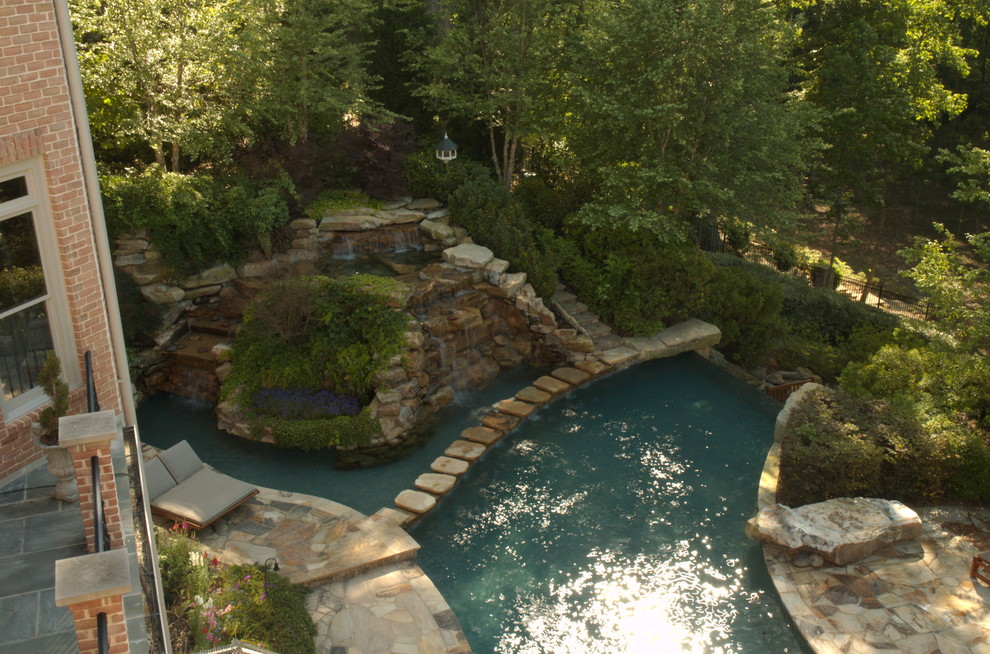 Photo of an expansive traditional backyard custom-shaped infinity pool in Atlanta with a water feature and natural stone pavers.