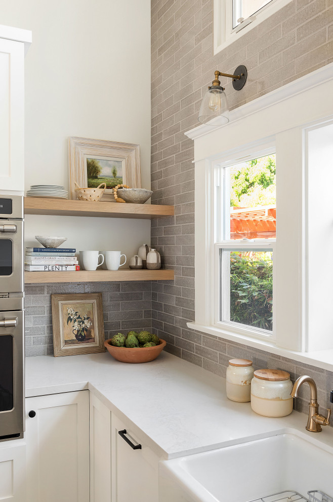 Mid-sized arts and crafts u-shaped open plan kitchen in San Diego with a farmhouse sink, shaker cabinets, white cabinets, quartz benchtops, grey splashback, ceramic splashback, stainless steel appliances, porcelain floors, with island, grey floor and white benchtop.